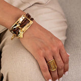 Chunky gold metal plate bracelet with brown leather strips, worn on a wrist, showcasing its bold design.