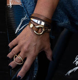 Brown leather wrap bracelet featuring honey gold double links and a chunky chain, worn stacked with a stylish ring.