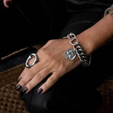 Chunky stainless steel bracelet featuring an ancient Greek coin pendant and a double lobster clasp, worn on a hand.