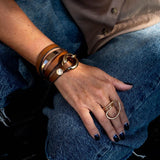 Brown leather wrap bracelet with honey gold double links, worn stacked with additional bracelets. Chunky design and adjustable fit.