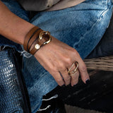 Brown leather wrap bracelet with honey gold double links, layered around the wrist, paired with a gold ring on hand.