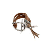 Western style bracelet featuring layered brown suede straps, a horsebit buckle, and a tassel detail.