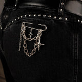 Silver safety pin brooch with chains and crosses displayed on black denim, adding an edgy, rock style accent.