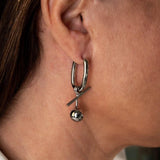 Asymmetrical drop earrings featuring a U-shaped design with a pearl and a metal ball, displayed on a model's ear.