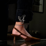 Silver safety pin brooch with chains and crosses, styled on the cuff of black jeans, paired with brown slingback heels.
