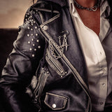 Silver safety pin brooch with chains and crosses styled on a black leather jacket, enhancing the rock aesthetic.