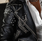 Silver safety pin brooch with chains and crosses attached to a studded black leather jacket, styled for a rock look.