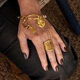 Chic gold bracelet with ball chain features a Greek coin and a unique design, worn on a hand with a chunky gold ring.