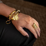 Chic gold bracelet with a ball chain and Greek coin, styled with other bangles, adds a layered look to the wrist.