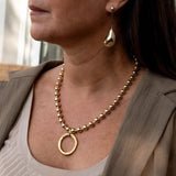 Chic gold bracelet with ball chain and Greek coin displayed on a woman's wrist, featuring a shiny, golden finish.