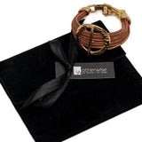 Hammered golden hoop bracelet with brown leather strands, featuring a bold, adjustable design and is presented in a black suede pouch.