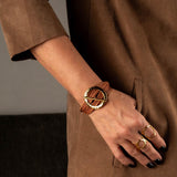 Chunky gold hoop bracelet with natural leather strands worn on a model's wrist, showcasing an edgy and stylish look.