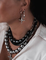 Silver hoop earrings with dangle cross and black enamel charms, styled on model with layered necklaces.