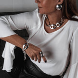 Oversized dome stud earrings with a polished metallic finish, worn with a chunky chain necklace and sleek clothing.