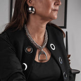 Oversized dome stud earrings in polished metallic finish, worn with a bold chain necklace and stylish black jacket.