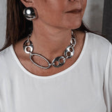 Oversized dome stud earrings in polished metallic finish, worn alongside a chunky silver necklace and simple white top.