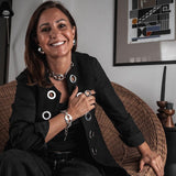 Oversized metallic dome stud earrings worn by a smiling woman, styled with a black jacket and additional jewelry.