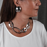 Oversized metallic dome stud earrings worn with a chunky chain necklace, both showcasing a polished finish.