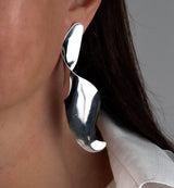 Sculptural silver statement stud earrings with an abstract wavy design, worn by a model, highlighting their bold look.