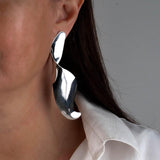Sculptural silver earrings with abstract wavy design, dangling from the model's ear, adding a bold touch to her outfit.