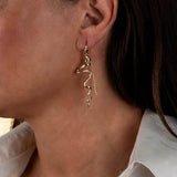 Asymmetrical gold earrings with a unique irregular pattern, hanging elegantly from the model's ear.