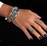 Multi-strand metal chain bracelet with chunky buckle, worn on a hand with silver rings and dark nail polish.