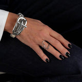 Multi-strand silver metal chain bracelet with a chunky buckle, worn on a hand with black nails and a minimalist ring.