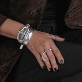 Multi-strand silver metal chain bracelet with chunky buckle, worn on a hand with black nail polish, paired with rings.