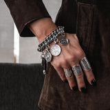 Chunky silver-plated chain bracelet featuring vintage coins and a leather closure, styled on a model’s wrist.
