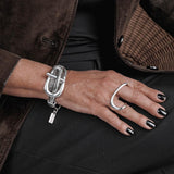 Multi-strand metal chain bracelet with a chunky buckle, worn on a wrist with a silver ring and stylish black nails.