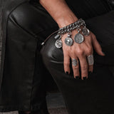 Chunky silver-plated bracelet with vintage coins, leather closure, worn on a hand resting on fitted black pants.