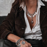 Chunky silver-plated chain bracelet with vintage coins and a leather closure, worn stacked with other bracelets.