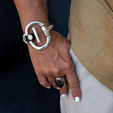 Hand wearing a silver bracelet and ring with a beige coat and white shirt.