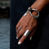Edgy metal and leather bracelet in silver, worn on a wrist with a unique irregular design and charm, paired with a chunky ring.