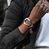 Edgy metal and leather bracelet featuring an irregular silver design with a charm, worn on a model's wrist.