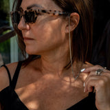 Thin silver chain necklace worn as a glasses holder, featuring black silicon loops for attachment. Model in a black top.