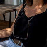 Thin, silver minimal chain necklace worn around the neck with glasses hanging from it; model is in a black top.
