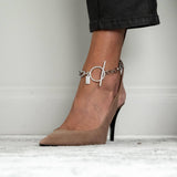 Bold chunky chain anklet in silver, featuring a T-clasp, worn on an ankle above a nude high heel shoe.
