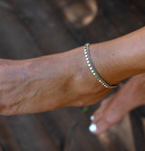 Dainty antique plated silver anklet with round charms, worn on a bare ankle, showcasing minimalistic elegance.