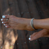 Silver antique-plated anklet with round charms, worn on a bare foot with polished white toenails, set on wooden floor.
