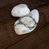 Stainless steel thick chain anklet with oval links, resting on smooth stones; versatile for both anklet and bracelet use.