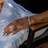 Thick stainless steel chain anklet/bracelet with oval links, worn layered on a model's wrist; minimalist and edgy design.