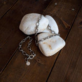 Thick stainless steel anklet featuring oval links, laid across smooth white stones on a wooden surface.