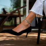 Stainless steel thick chain anklet with oval links, worn around the ankle, paired with a black heeled shoe.