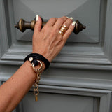 Double link metal bracelet in honey gold and black leather, featuring chunky links and a soft black leather wrap.