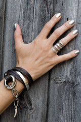 Chunky double link metal bracelet in honey gold with black leather wrap, showcased on a hand against a wooden background.