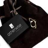 Irregular shaped statement ring in metallic copper displayed on a dark brown suede pouch with a logo tag.