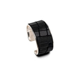 Wide brass cuff bracelet features embossed black leather with a subtle animal print, suitable for stacking or solo wear.