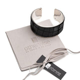 Wide metal cuff bracelet featuring dark brown embossed leather with animal print. Adjustable design, set on a suede pouch.