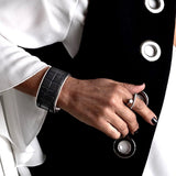 Wide brass cuff bracelet featuring dark brown embossed leather with an animal print, stylishly worn on a model's wrist.
